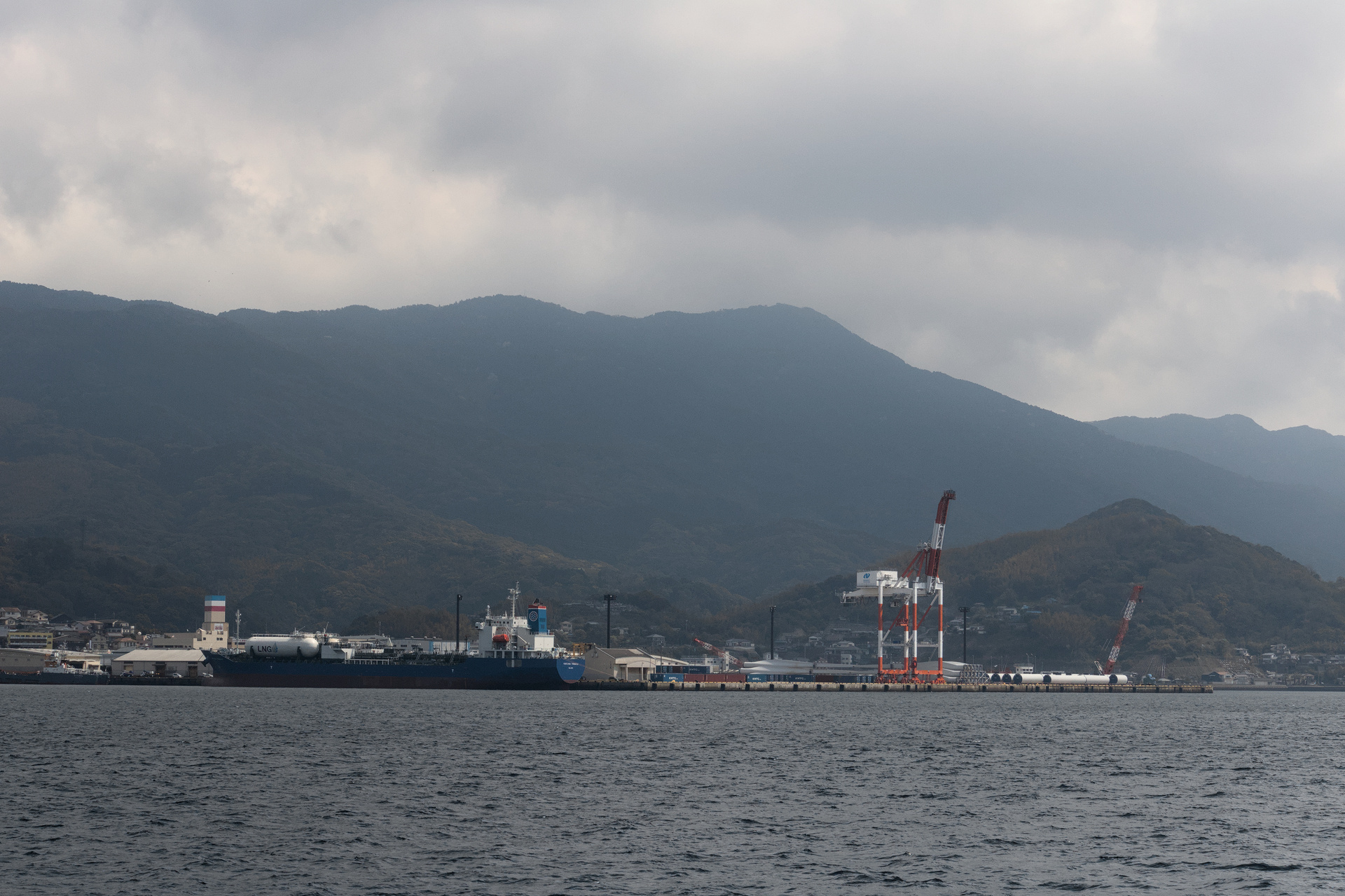 Foggy industrial dock with tall mountains in the background fading into the clouds.